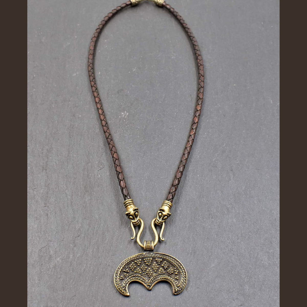 Lunula-Lederkette mit Rabenköpfen
Zwei kunstvoll verzierte Rabenköpfe halten einen Omega-Haken, an dem ein halbmondförmiger Lunula-Anhänger befestigt ist. Die geflochtene Lederkette verbindet damit zwei unterschiedliche historische Schmuckvorbilder aus der Wikingerzeit.