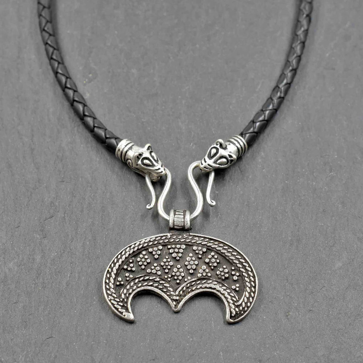 Lunula-Lederkette mit Rabenköpfen
Zwei kunstvoll verzierte Rabenköpfe halten einen Omega-Haken, an dem ein halbmondförmiger Lunula-Anhänger befestigt ist. Die geflochtene Lederkette verbindet damit zwei unterschiedliche historische Schmuckvorbilder aus der Wikingerzeit.
