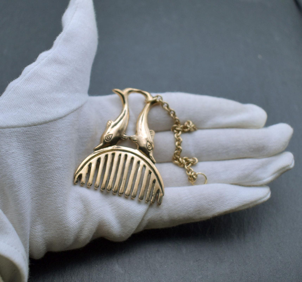Römischer Bartkamm mit Delphinen aus Bronze an einer Kette auf der Hand