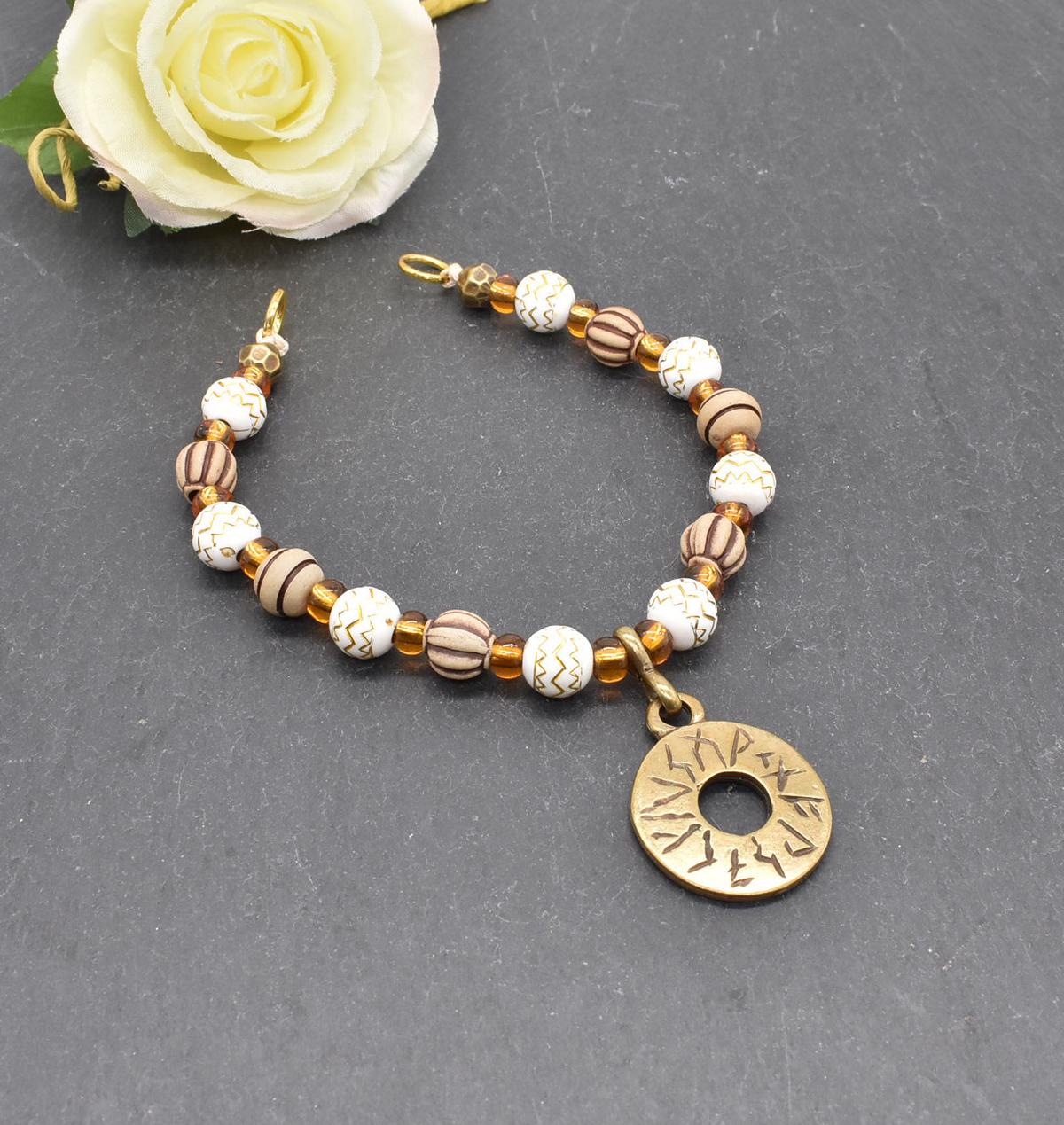 Handgefertigte Runen Fibelkette von BELANAS SCHATZKISTE mit hellbraunen und weißen Acrylperlen, goldfarbenen Mustern, braunen Goldfolienperlen und einem runden Runenamulett aus ZAMAK. Elegantes Design mit mystischem Wikinger-Charme.