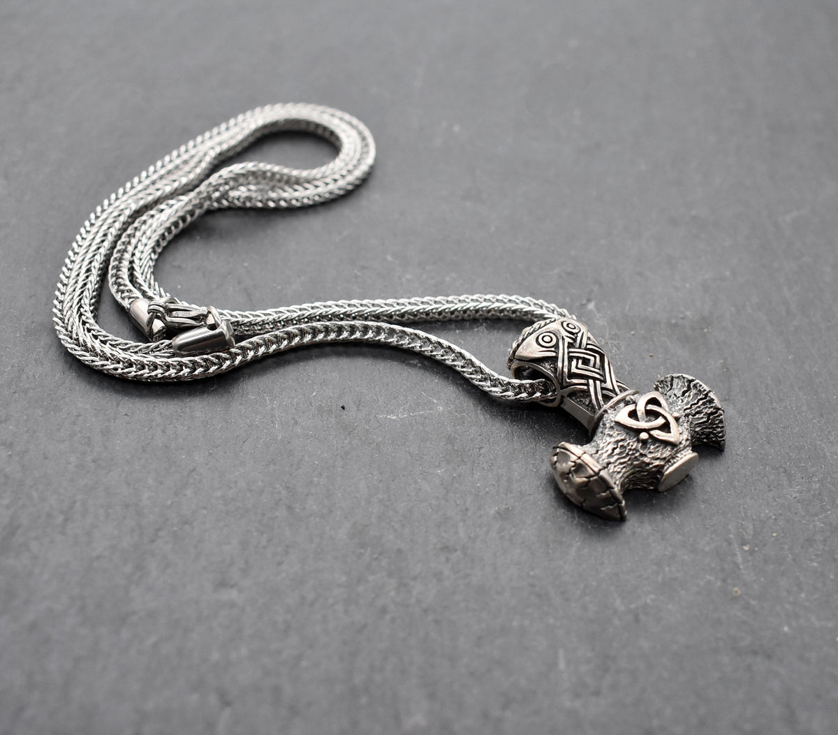 Thorshammer-Kette aus 925er Sterling Silber
Der massiv gearbeitete Thorshammer aus 925er Sterling Silber ist der Mittelpunkt dieser nordisch inspirierten Halskette.
Verschlungene Flechtornamente verzieren den Schaft des Mjölnir, während auf dem Hammerkopf eine Triskele sitzt. Die Vertiefungen sind dunkel abgesetzt und lassen die plastischen Details des Silberanhängers deutlich hervortreten.
Kombiniert ist der etwa 8,5 g schwere Anhänger mit einer 56 cm langen Fuchsschwanzkette aus Edelstahl. Geschlossen