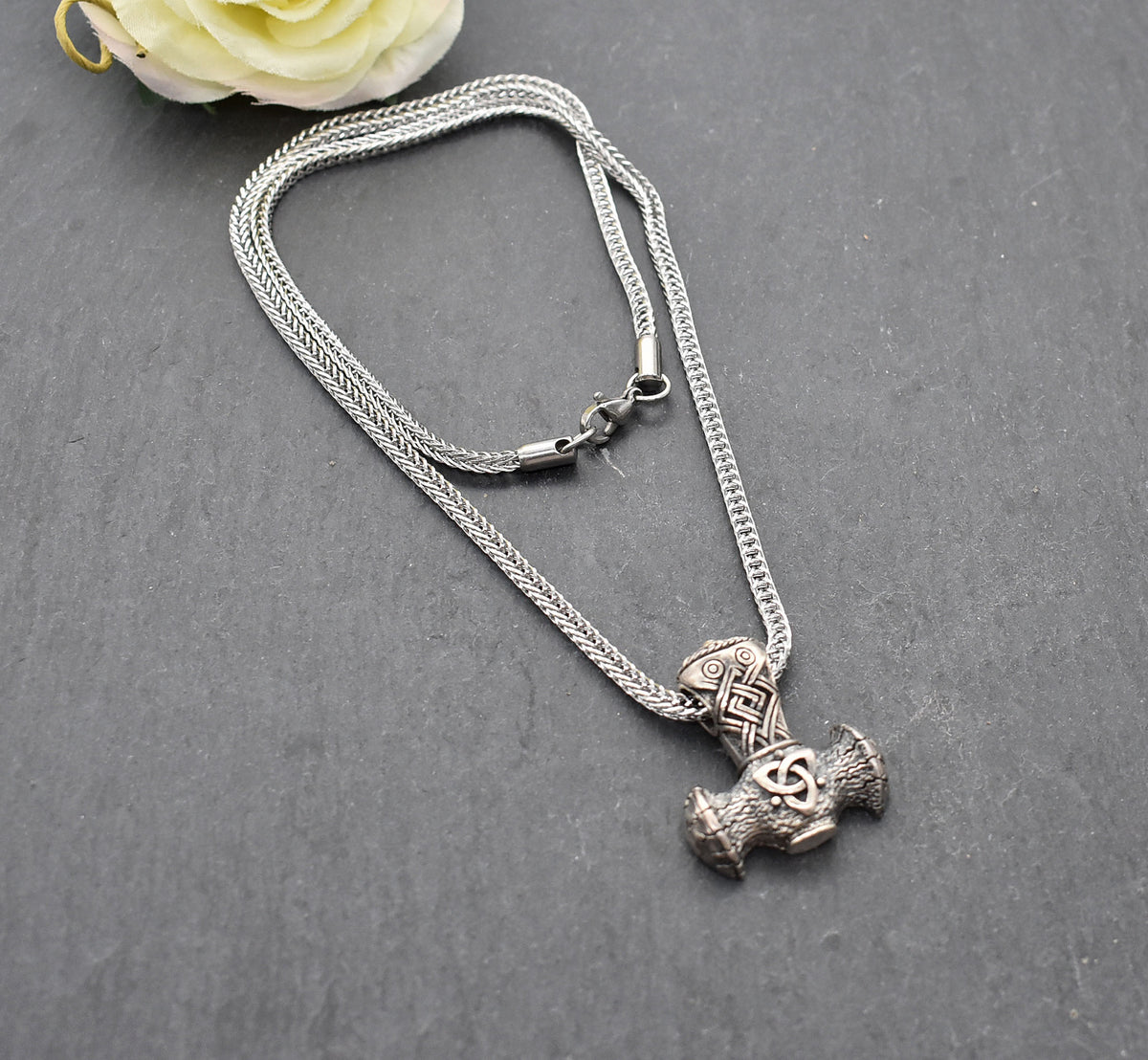Thorshammer-Kette aus 925er Sterling Silber
Der massiv gearbeitete Thorshammer aus 925er Sterling Silber ist der Mittelpunkt dieser nordisch inspirierten Halskette.
Verschlungene Flechtornamente verzieren den Schaft des Mjölnir, während auf dem Hammerkopf eine Triskele sitzt. Die Vertiefungen sind dunkel abgesetzt und lassen die plastischen Details des Silberanhängers deutlich hervortreten.
Kombiniert ist der etwa 8,5 g schwere Anhänger mit einer 56 cm langen Fuchsschwanzkette aus Edelstahl. Geschlossen