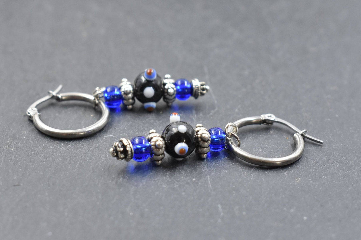 Creolen mit Lampwork Anhänger in schwarz und blau liegend auf einer Schieferplatte