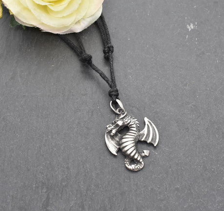 Detailreiner Drachenanhänger aus Zinn an schwarzem Textilband auf dunklem Schieferhintergrund.