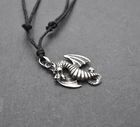 Detailreiner Drachenanhänger aus Zinn an schwarzem Textilband auf dunklem Schieferhintergrund.