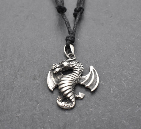 Detailreiner Drachenanhänger aus Zinn an schwarzem Textilband auf dunklem Schieferhintergrund.