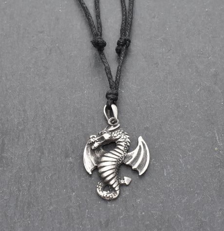 Detailreiner Drachenanhänger aus Zinn an schwarzem Textilband auf dunklem Schieferhintergrund.