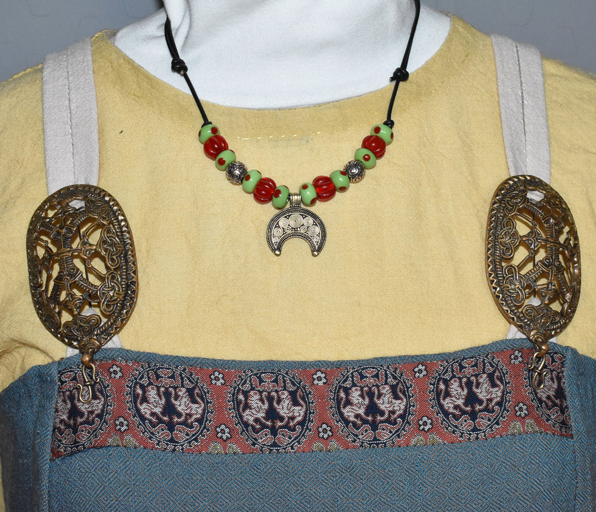 Tragebild am Wikinger Kleid der Historische Lunula Halskette VENUS aus Bronze mit handgefertigten roten und grünen Glasperlen. Perfekt für Mittelalter, Reenactment und LARP. Verstellbares Lederband, authentischer römischer Schmuck.