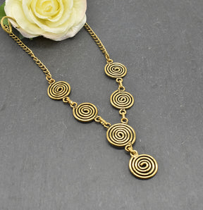 Die Keltische Bronzekette Alin ist ein handgefertigtes Schmuckstück aus hochwertigem Bronzedraht. Das Design besticht durch elegante, runde Spiralen, die mit filigranen Kettengliedern verbunden sind. Der edle bronzene Farbton verleiht der Kette eine zeitlose, mystische Ausstrahlung. Mit einer Länge von etwa 53 cm und einem praktischen Hakenverschluss eignet sich die Kette perfekt für den Alltag oder als besonderes Accessoire zu eleganten Outfits wie Blusen oder Rollkragenpullovern. Ideal für alle, die kelti