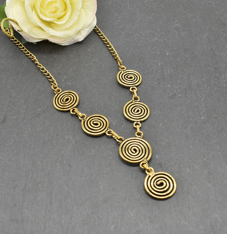 Die Keltische Bronzekette Alin ist ein handgefertigtes Schmuckstück aus hochwertigem Bronzedraht. Das Design besticht durch elegante, runde Spiralen, die mit filigranen Kettengliedern verbunden sind. Der edle bronzene Farbton verleiht der Kette eine zeitlose, mystische Ausstrahlung. Mit einer Länge von etwa 53 cm und einem praktischen Hakenverschluss eignet sich die Kette perfekt für den Alltag oder als besonderes Accessoire zu eleganten Outfits wie Blusen oder Rollkragenpullovern. Ideal für alle, die kelti