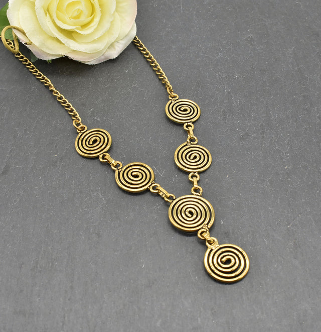 Die Keltische Bronzekette Alin ist ein handgefertigtes Schmuckstück aus hochwertigem Bronzedraht. Das Design besticht durch elegante, runde Spiralen, die mit filigranen Kettengliedern verbunden sind. Der edle bronzene Farbton verleiht der Kette eine zeitlose, mystische Ausstrahlung. Mit einer Länge von etwa 53 cm und einem praktischen Hakenverschluss eignet sich die Kette perfekt für den Alltag oder als besonderes Accessoire zu eleganten Outfits wie Blusen oder Rollkragenpullovern. Ideal für alle, die kelti