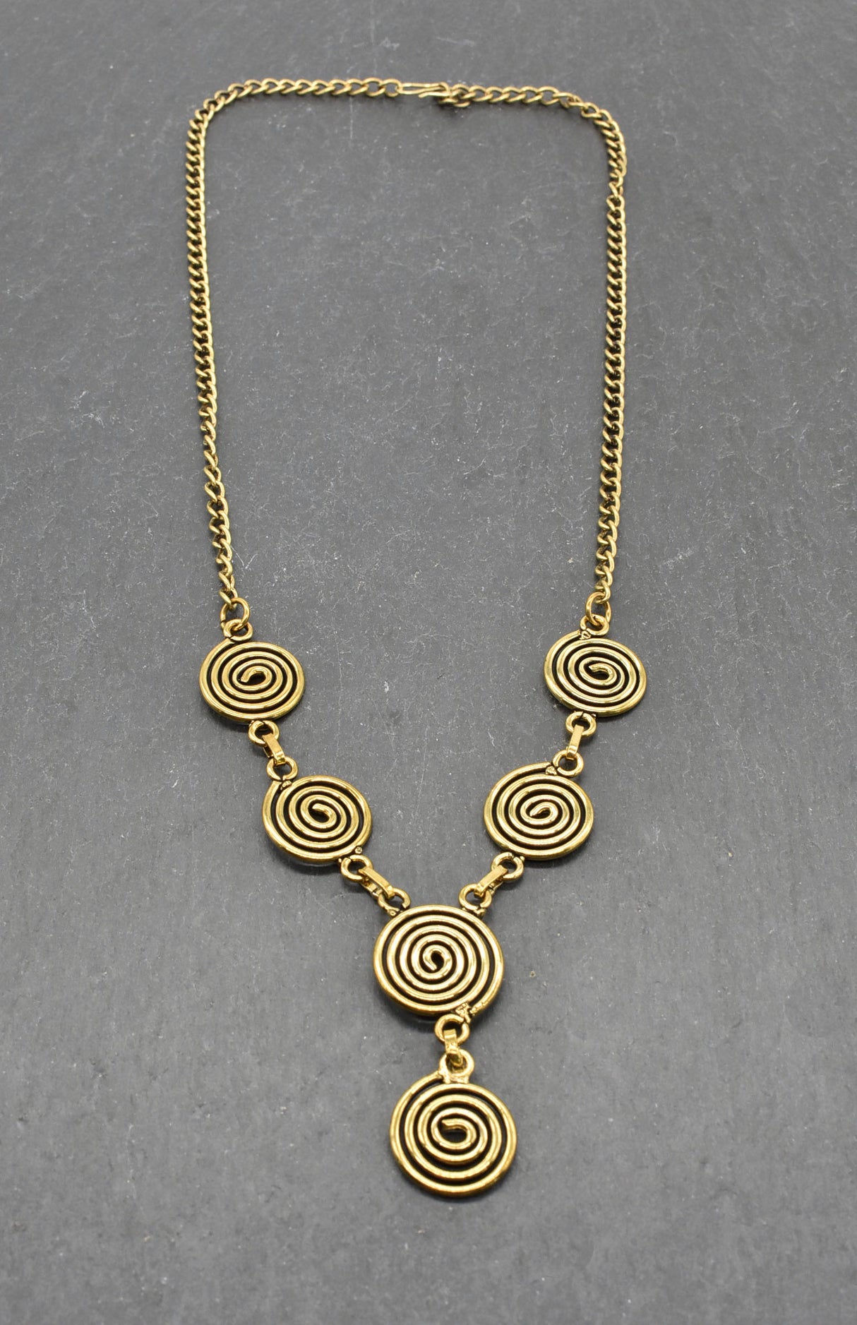 Die Keltische Bronzekette Alin ist ein handgefertigtes Schmuckstück aus hochwertigem Bronzedraht. Das Design besticht durch elegante, runde Spiralen, die mit filigranen Kettengliedern verbunden sind. Der edle bronzene Farbton verleiht der Kette eine zeitlose, mystische Ausstrahlung. Mit einer Länge von etwa 53 cm und einem praktischen Hakenverschluss eignet sich die Kette perfekt für den Alltag oder als besonderes Accessoire zu eleganten Outfits wie Blusen oder Rollkragenpullovern. Ideal für alle, die kelti