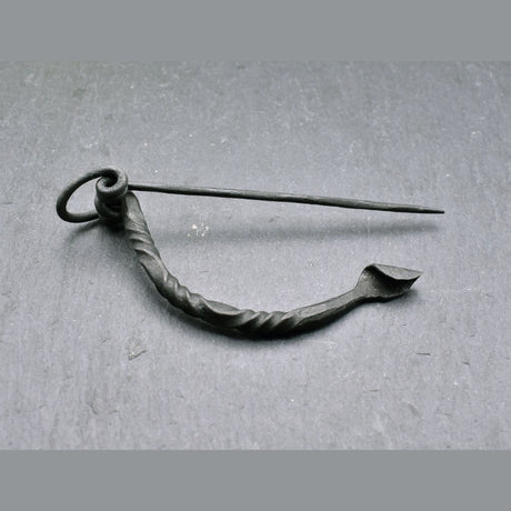 Keltische Bügelfibel aus Eisen – handgeschmiedete Latène-Fibel

Diese keltische Bügelfibel aus Eisen ist von Hand geschmiedet und orientiert sich an historischen Fibelformen der Latènezeit. Der kräftige Bügel ist teilweise tordiert und geht in eine Spiralkonstruktion mit langer Nadel über. Am anderen Ende befindet sich der Nadelhalter, in den die Spitze zum Verschließen des Stoffes eingelegt wird.
