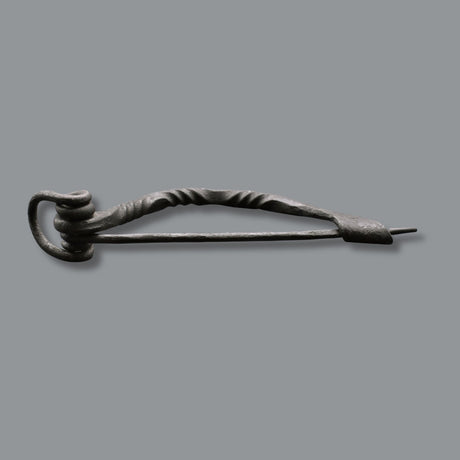 Keltische Bügelfibel aus Eisen – handgeschmiedete Latène-Fibel

Diese keltische Bügelfibel aus Eisen ist von Hand geschmiedet und orientiert sich an historischen Fibelformen der Latènezeit. Der kräftige Bügel ist teilweise tordiert und geht in eine Spiralkonstruktion mit langer Nadel über. Am anderen Ende befindet sich der Nadelhalter, in den die Spitze zum Verschließen des Stoffes eingelegt wird.