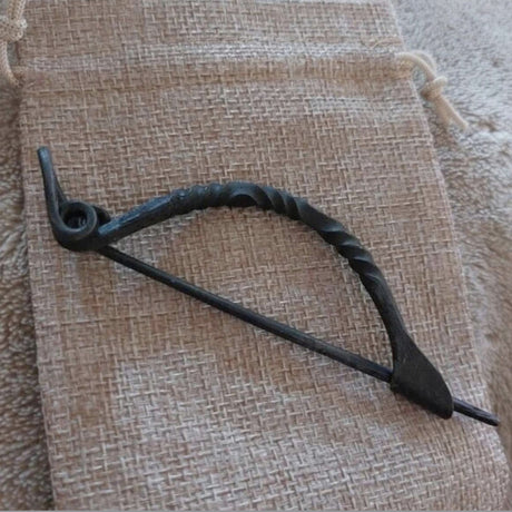 Keltische Bügelfibel aus Eisen – handgeschmiedete Latène-Fibel

Diese keltische Bügelfibel aus Eisen ist von Hand geschmiedet und orientiert sich an historischen Fibelformen der Latènezeit. Der kräftige Bügel ist teilweise tordiert und geht in eine Spiralkonstruktion mit langer Nadel über. Am anderen Ende befindet sich der Nadelhalter, in den die Spitze zum Verschließen des Stoffes eingelegt wird.