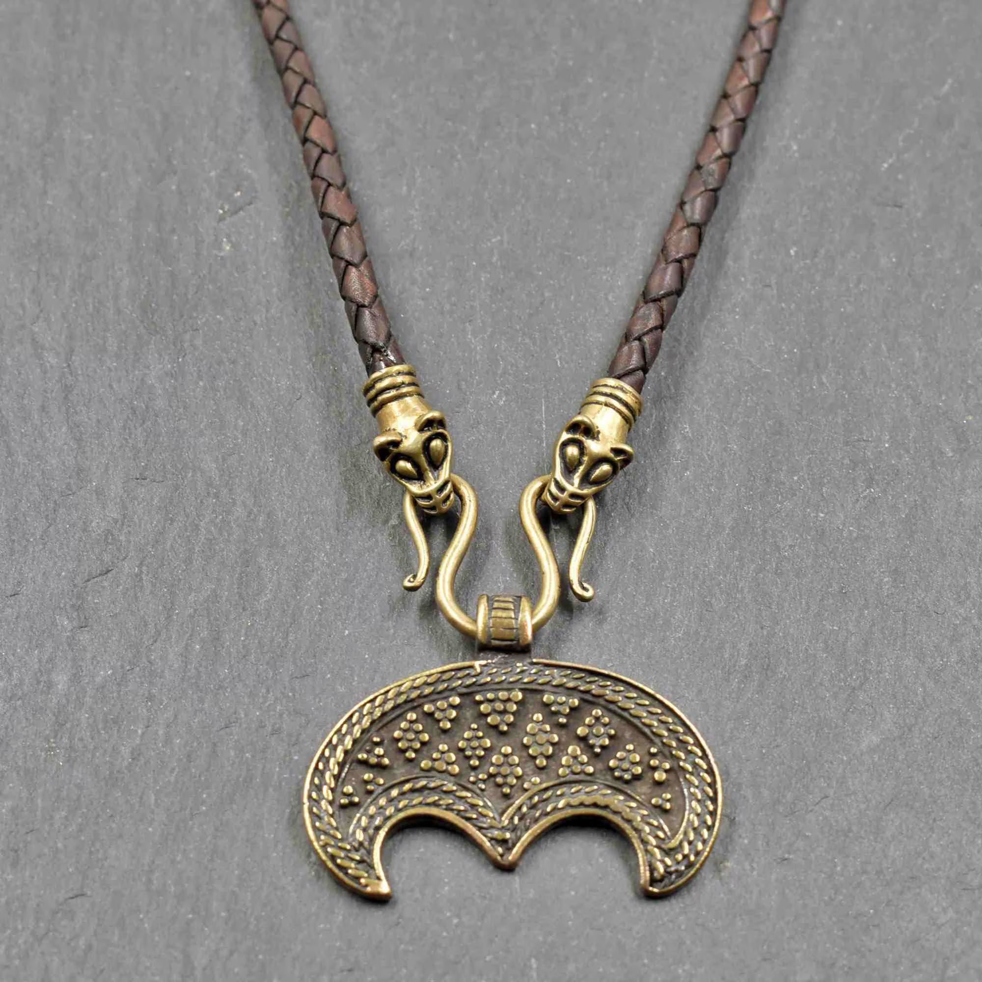 Lunula-Lederkette mit Rabenköpfen

Zwei kunstvoll verzierte Rabenköpfe halten einen Omega-Haken, an dem ein halbmondförmiger Lunula-Anhänger befestigt ist. Die geflochtene Lederkette verbindet damit zwei unterschiedliche historische Schmuckvorbilder aus der Wikingerzeit.