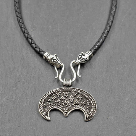 Lunula-Lederkette mit Rabenköpfen

Zwei kunstvoll verzierte Rabenköpfe halten einen Omega-Haken, an dem ein halbmondförmiger Lunula-Anhänger befestigt ist. Die geflochtene Lederkette verbindet damit zwei unterschiedliche historische Schmuckvorbilder aus der Wikingerzeit.