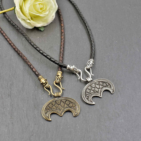Lunula-Lederketten mit Rabenköpfen

Zwei kunstvoll verzierte Rabenköpfe halten einen Omega-Haken, an dem ein halbmondförmiger Lunula-Anhänger befestigt ist. Die geflochtene Lederkette in braun oder schwarz verbindet damit zwei unterschiedliche historische Lunulas aus Bronze oder Silber.
