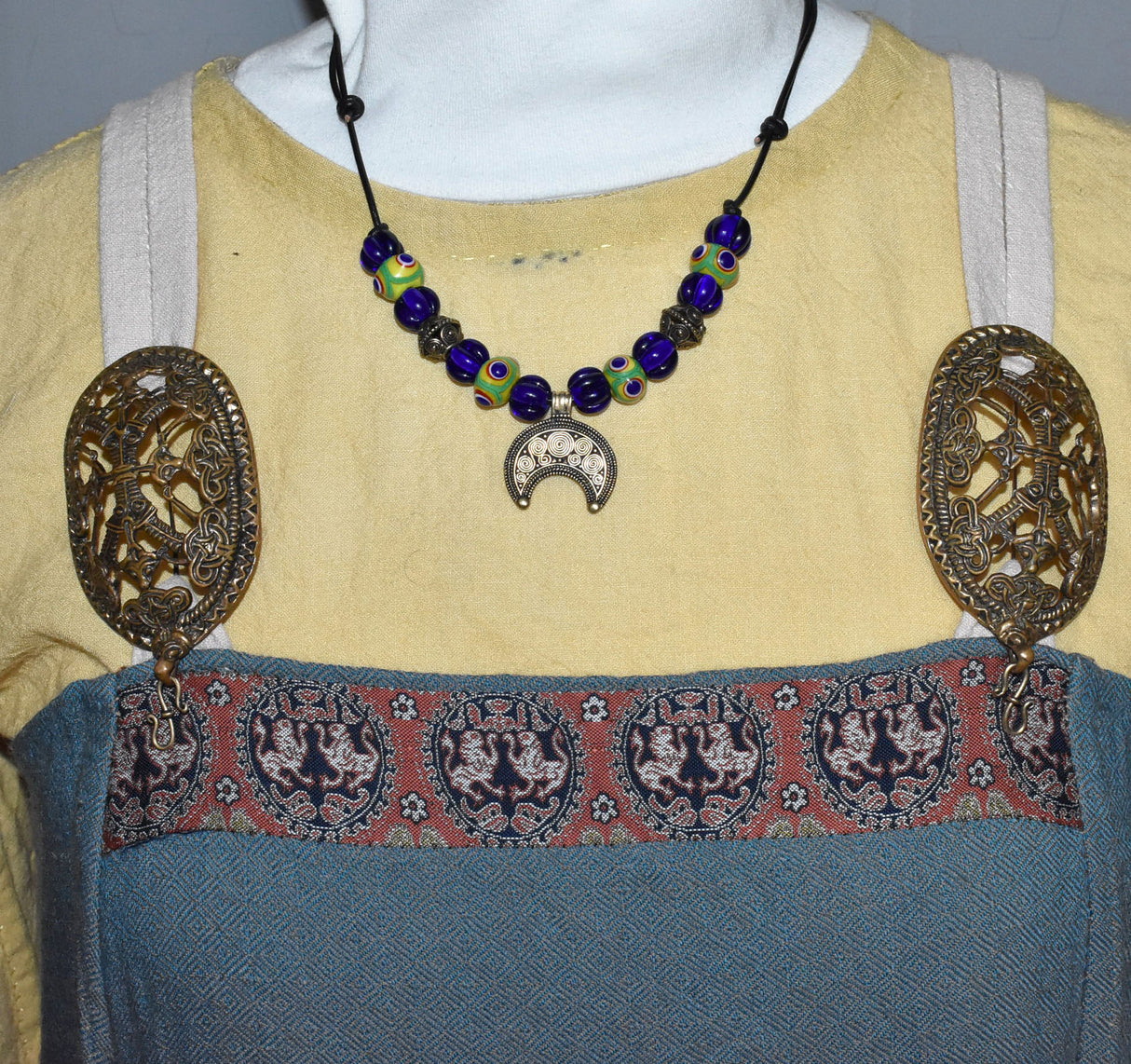 Tragebild am Wikingergewand der Lunula Halskette NOVA – Römisches Bronze Mondamulet mit handgefertigten Lampwork Glasperlen in Blau und Grün-Gelb