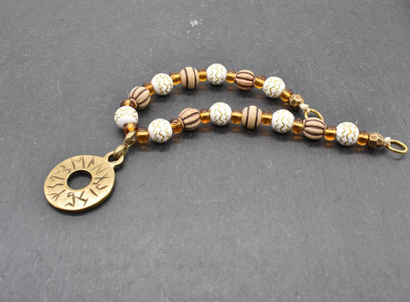 Handgefertigte Runen Fibelkette von BELANAS SCHATZKISTE mit hellbraunen und weißen Acrylperlen, goldfarbenen Mustern, braunen Goldfolienperlen und einem runden Runenamulett aus ZAMAK. Elegantes Design mit mystischem Wikinger-Charme.