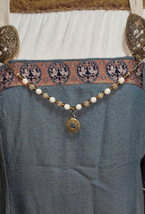 Tragebild am Wikingerkleid der Handgefertigte Runen Fibelkette von BELANAS SCHATZKISTE mit hellbraunen und weißen Acrylperlen, goldfarbenen Mustern, braunen Goldfolienperlen und einem runden Runenamulett aus ZAMAK. Elegantes Design mit mystischem Wikinger-Charme.