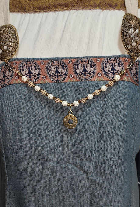 Tragebild am Wikingerkleid der Handgefertigte Runen Fibelkette von BELANAS SCHATZKISTE mit hellbraunen und weißen Acrylperlen, goldfarbenen Mustern, braunen Goldfolienperlen und einem runden Runenamulett aus ZAMAK. Elegantes Design mit mystischem Wikinger-Charme.