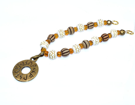 Handgefertigte Runen Fibelkette von BELANAS SCHATZKISTE mit hellbraunen und weißen Acrylperlen, goldfarbenen Mustern, braunen Goldfolienperlen und einem runden Runenamulett aus ZAMAK. Elegantes Design mit mystischem Wikinger-Charme.