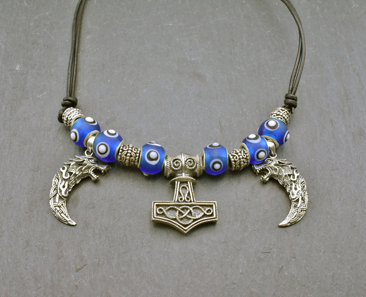 Mjölnir-Kette „Ragnar“ kombiniert drei Anhänger aus 925er Sterling Silber mit kräftig blauen, handgefertigten Glasperlen und schwarzem Lederband.

Im Mittelpunkt sitzt ein reich verzierter Thorshammer. Zwei gebogene, zahnförmige Anhänger mit plastisch ausgearbeiteten Wolfsköpfen flankieren den Mjölnir.