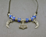 Mjölnir-Kette „Ragnar“ kombiniert drei Anhänger aus 925er Sterling Silber mit kräftig blauen, handgefertigten Glasperlen und schwarzem Lederband.

Im Mittelpunkt sitzt ein reich verzierter Thorshammer. Zwei gebogene, zahnförmige Anhänger mit plastisch ausgearbeiteten Wolfsköpfen flankieren den Mjölnir.