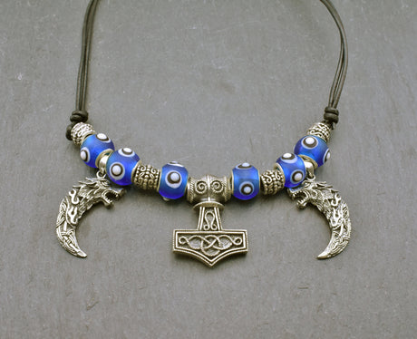 Mjölnir-Kette „Ragnar“ kombiniert drei Anhänger aus 925er Sterling Silber mit kräftig blauen, handgefertigten Glasperlen und schwarzem Lederband.

Im Mittelpunkt sitzt ein reich verzierter Thorshammer. Zwei gebogene, zahnförmige Anhänger mit plastisch ausgearbeiteten Wolfsköpfen flankieren den Mjölnir.