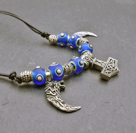 Mjölnir-Kette „Ragnar“ kombiniert drei Anhänger aus 925er Sterling Silber mit kräftig blauen, handgefertigten Glasperlen und schwarzem Lederband.

Im Mittelpunkt sitzt ein reich verzierter Thorshammer. Zwei gebogene, zahnförmige Anhänger mit plastisch ausgearbeiteten Wolfsköpfen flankieren den Mjölnir.
