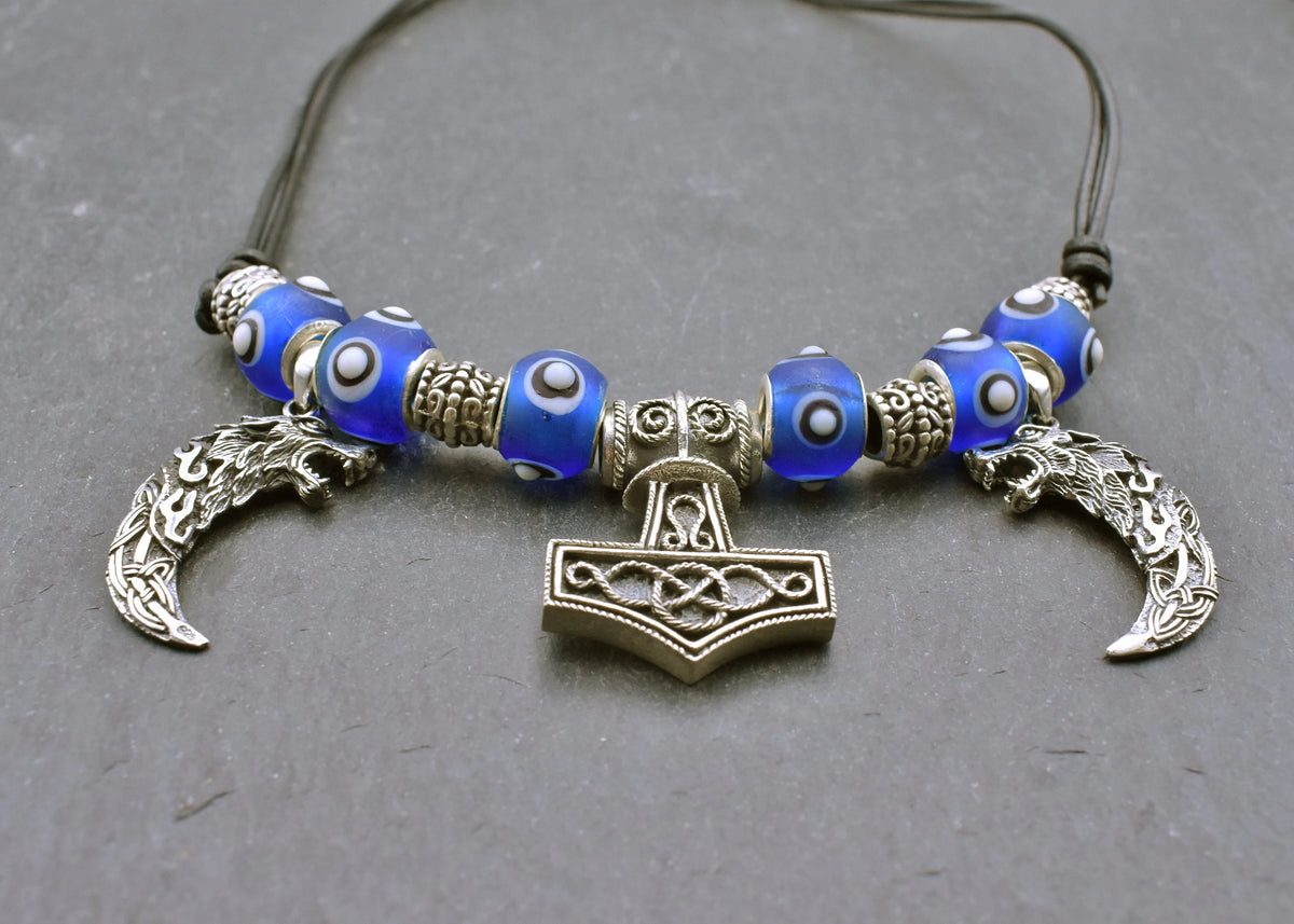 Mjölnir-Kette „Ragnar“ kombiniert drei Anhänger aus 925er Sterling Silber mit kräftig blauen, handgefertigten Glasperlen und schwarzem Lederband.

Im Mittelpunkt sitzt ein reich verzierter Thorshammer. Zwei gebogene, zahnförmige Anhänger mit plastisch ausgearbeiteten Wolfsköpfen flankieren den Mjölnir.