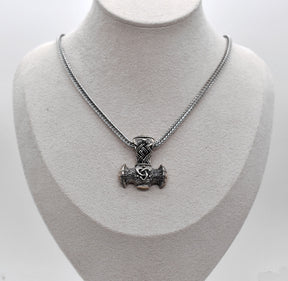 Thorshammer-Kette aus 925er Sterling Silber

Der massiv gearbeitete Thorshammer aus 925er Sterling Silber ist der Mittelpunkt dieser nordisch inspirierten Halskette.

Verschlungene Flechtornamente verzieren den Schaft des Mjölnir, während auf dem Hammerkopf eine Triskele sitzt. Die Vertiefungen sind dunkel abgesetzt und lassen die plastischen Details des Silberanhängers deutlich hervortreten.

Kombiniert ist der etwa 8,5 g schwere Anhänger mit einer 56 cm langen Fuchsschwanzkette aus Edelstahl. Geschlossen 