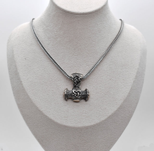 Thorshammer-Kette aus 925er Sterling Silber

Der massiv gearbeitete Thorshammer aus 925er Sterling Silber ist der Mittelpunkt dieser nordisch inspirierten Halskette.

Verschlungene Flechtornamente verzieren den Schaft des Mjölnir, während auf dem Hammerkopf eine Triskele sitzt. Die Vertiefungen sind dunkel abgesetzt und lassen die plastischen Details des Silberanhängers deutlich hervortreten.

Kombiniert ist der etwa 8,5 g schwere Anhänger mit einer 56 cm langen Fuchsschwanzkette aus Edelstahl. Geschlossen 