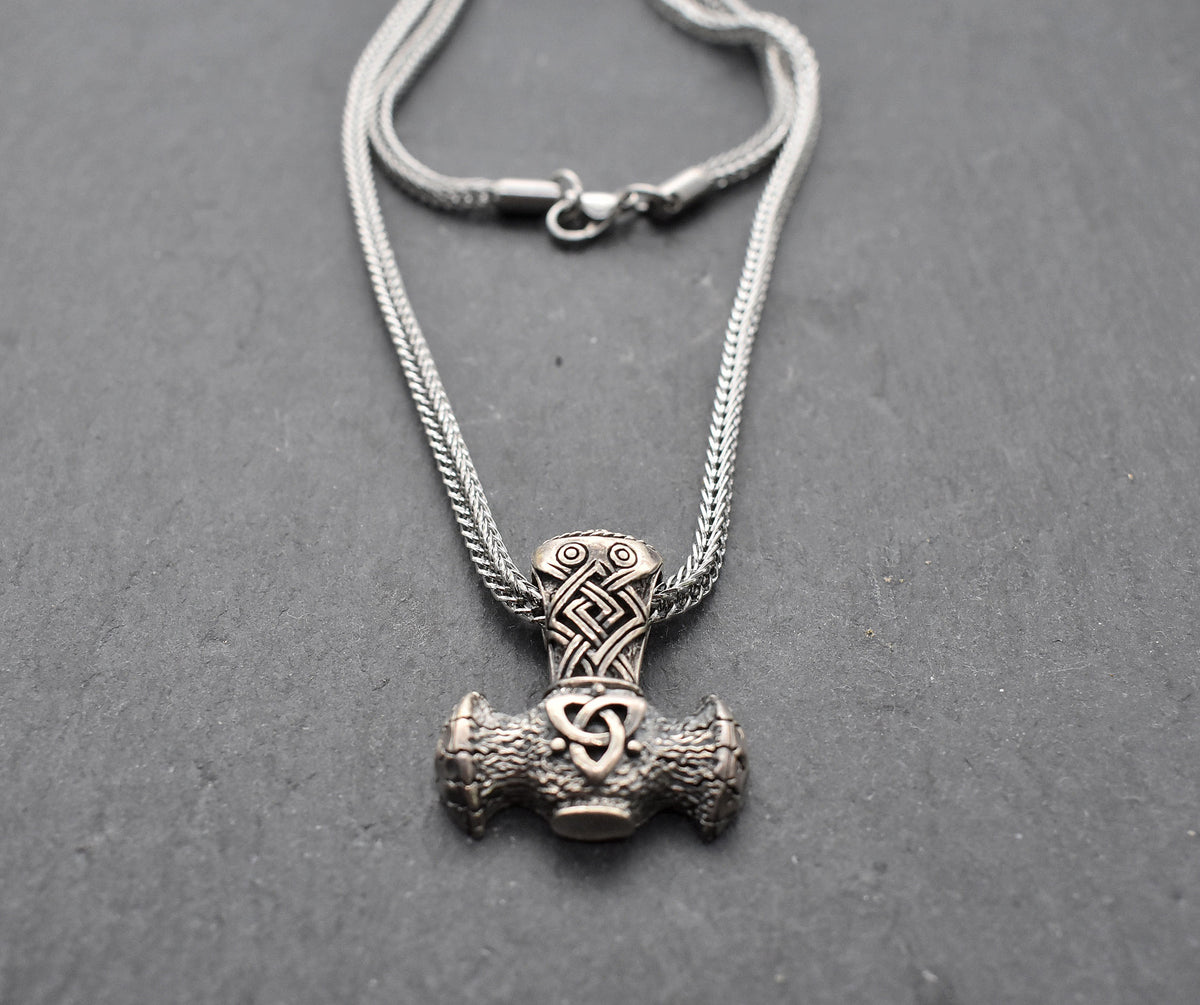 Thorshammer-Kette aus 925er Sterling Silber

Der massiv gearbeitete Thorshammer aus 925er Sterling Silber ist der Mittelpunkt dieser nordisch inspirierten Halskette.

Verschlungene Flechtornamente verzieren den Schaft des Mjölnir, während auf dem Hammerkopf eine Triskele sitzt. Die Vertiefungen sind dunkel abgesetzt und lassen die plastischen Details des Silberanhängers deutlich hervortreten.

Kombiniert ist der etwa 8,5 g schwere Anhänger mit einer 56 cm langen Fuchsschwanzkette aus Edelstahl. Geschlossen 