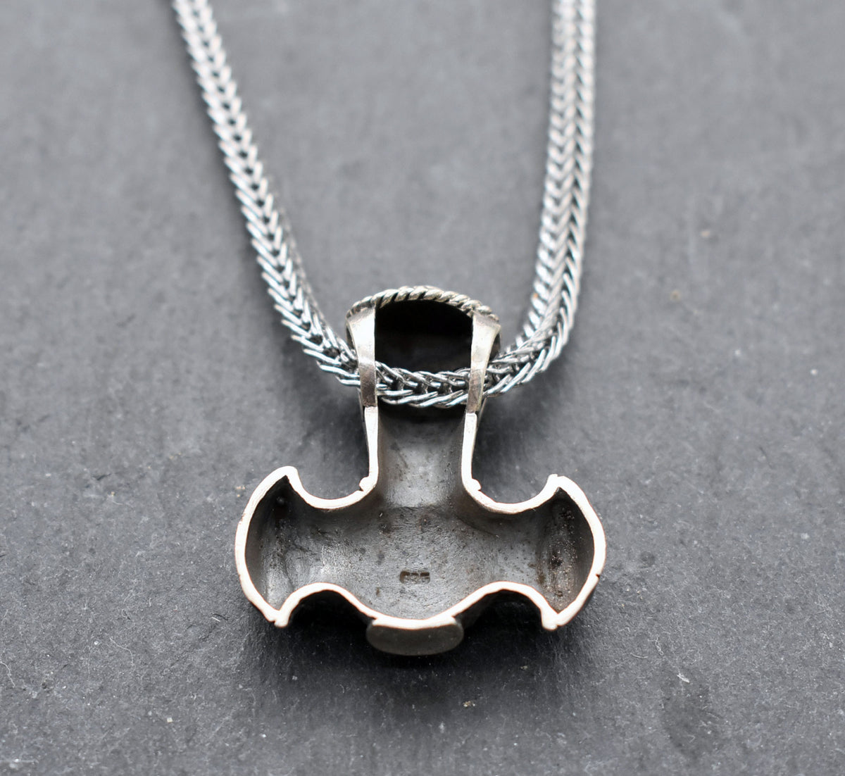 Rückseite mit Stempel der Thorshammer-Kette aus 925er Sterling Silber

Der massiv gearbeitete Thorshammer aus 925er Sterling Silber ist der Mittelpunkt dieser nordisch inspirierten Halskette.

Verschlungene Flechtornamente verzieren den Schaft des Mjölnir, während auf dem Hammerkopf eine Triskele sitzt. Die Vertiefungen sind dunkel abgesetzt und lassen die plastischen Details des Silberanhängers deutlich hervortreten.

Kombiniert ist der etwa 8,5 g schwere Anhänger mit einer 56 cm langen Fuchsschwanzkette a