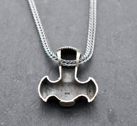 Rückseite mit Stempel der Thorshammer-Kette aus 925er Sterling Silber

Der massiv gearbeitete Thorshammer aus 925er Sterling Silber ist der Mittelpunkt dieser nordisch inspirierten Halskette.

Verschlungene Flechtornamente verzieren den Schaft des Mjölnir, während auf dem Hammerkopf eine Triskele sitzt. Die Vertiefungen sind dunkel abgesetzt und lassen die plastischen Details des Silberanhängers deutlich hervortreten.

Kombiniert ist der etwa 8,5 g schwere Anhänger mit einer 56 cm langen Fuchsschwanzkette a