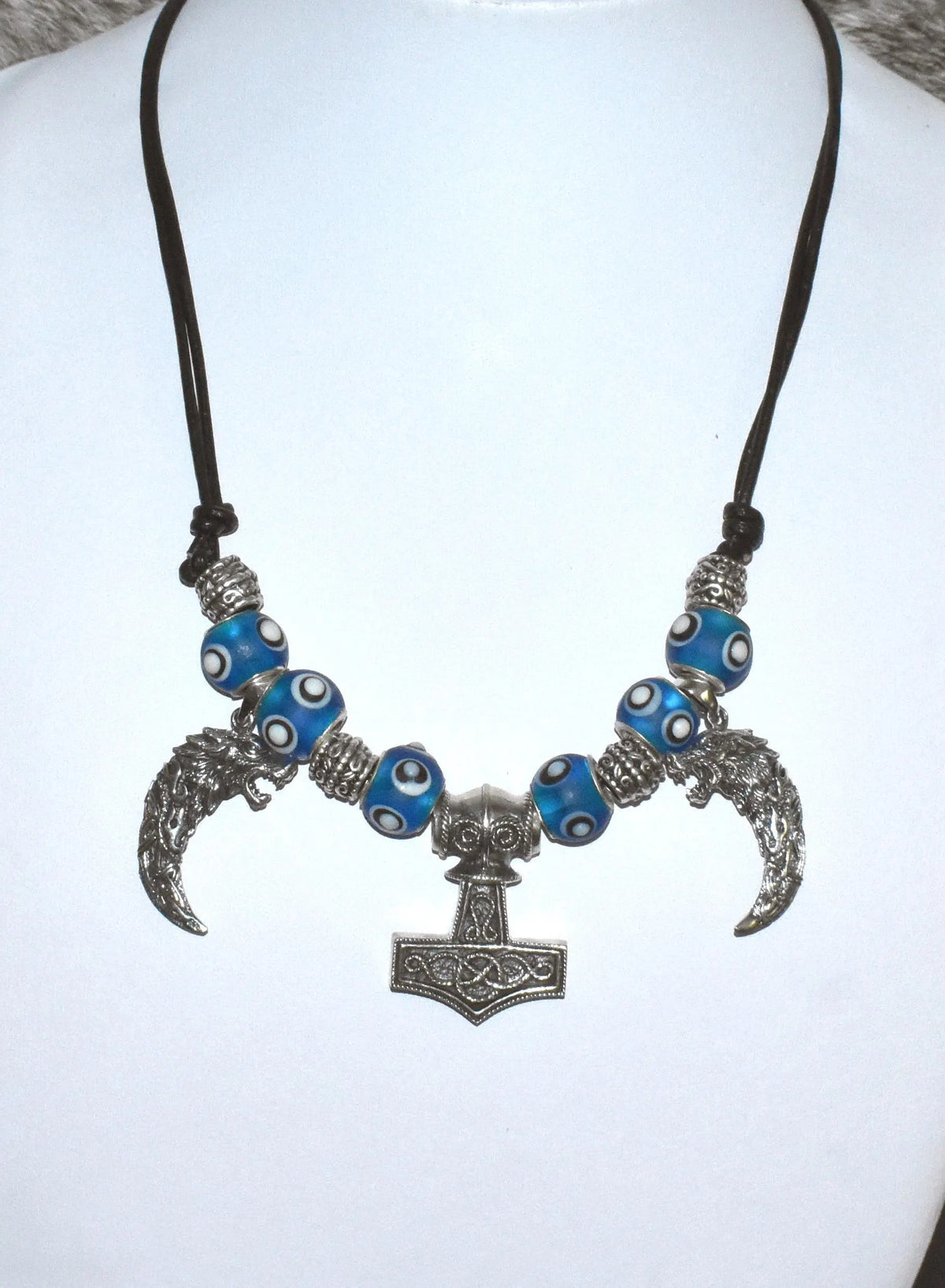 Mjölnir-Kette „Ragnar“ kombiniert drei Anhänger aus 925er Sterling Silber mit kräftig blauen, handgefertigten Glasperlen und schwarzem Lederband.

Im Mittelpunkt sitzt ein reich verzierter Thorshammer. Zwei gebogene, zahnförmige Anhänger mit plastisch ausgearbeiteten Wolfsköpfen flankieren den Mjölnir.