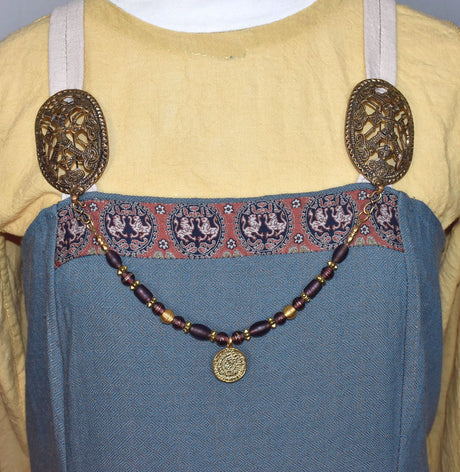 Tragebild am Wikinger-Kleid der Wikinger Fibelkette Maijvi mit dunkel-lila Glasperlen und vergoldetem Münzanhänger