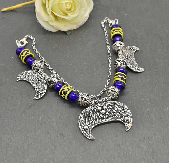 Lunula Fibelkette INGRID mit dunkelblauen Glasperlen mit gelbem Muster, sowie silbernen Perlen und Anhängern auf einer Schieferplatte mit gelber Rose
