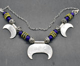 Rückseite der Lunula Fibelkette INGRID mit dunkelblauen Glasperlen mit gelbem Muster, sowie silbernen Perlen und Anhängern auf einer Schieferplatte 
