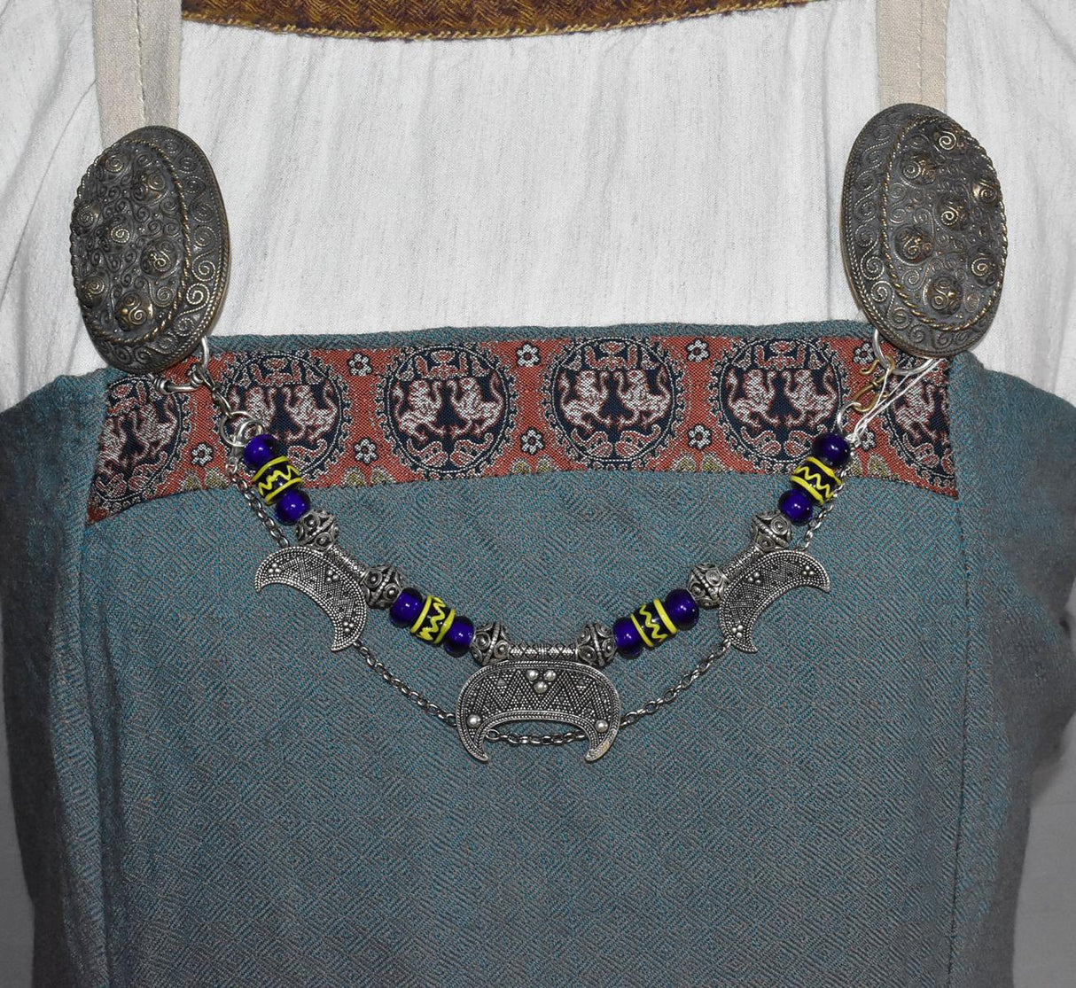 Lunula Fibelkette INGRID mit dunkelblauen Glasperlen mit gelbem Muster, sowie silbernen Perlen und Anhängern am Wikingerkleid