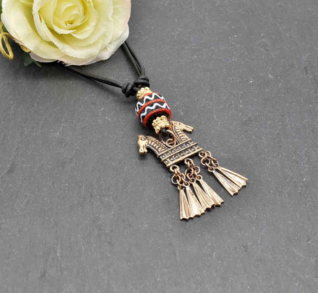 Keltische Halskette Echna aus Bronze, mit handgefertigter schwarzer Glasperle mit Muster aus rot und weiß, sowie vergoldeten Metallperlen an einem verstellbaren Lederband.