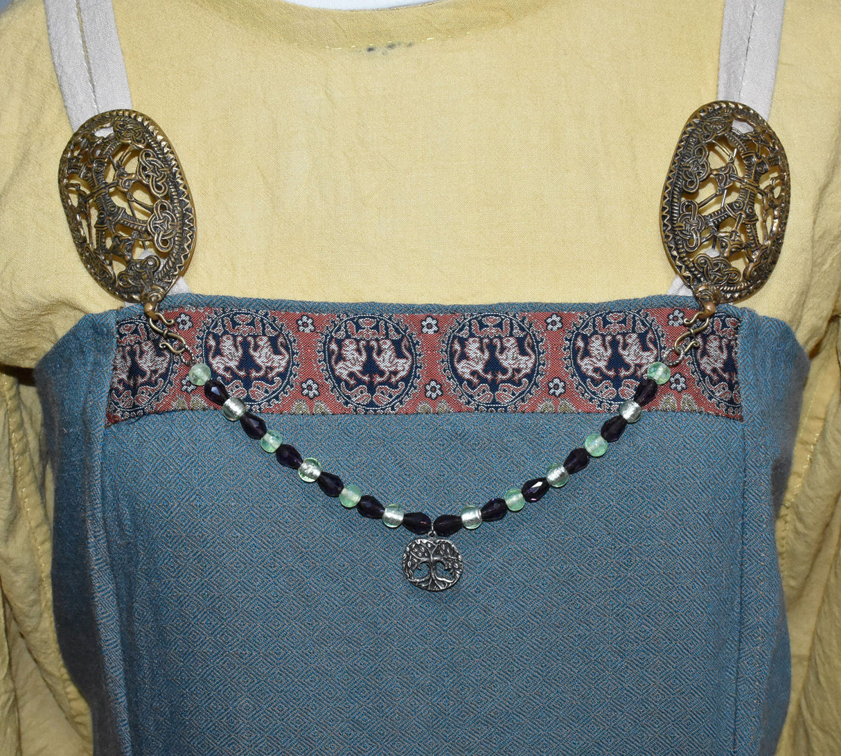 Tragebild am Wikingerkleid der Yggdrasil Fibelkette im Wikinger-Stil – Handgefertigt mit silberfarbenem Anhänger und Glasperlen in hellgrün und dunkellila