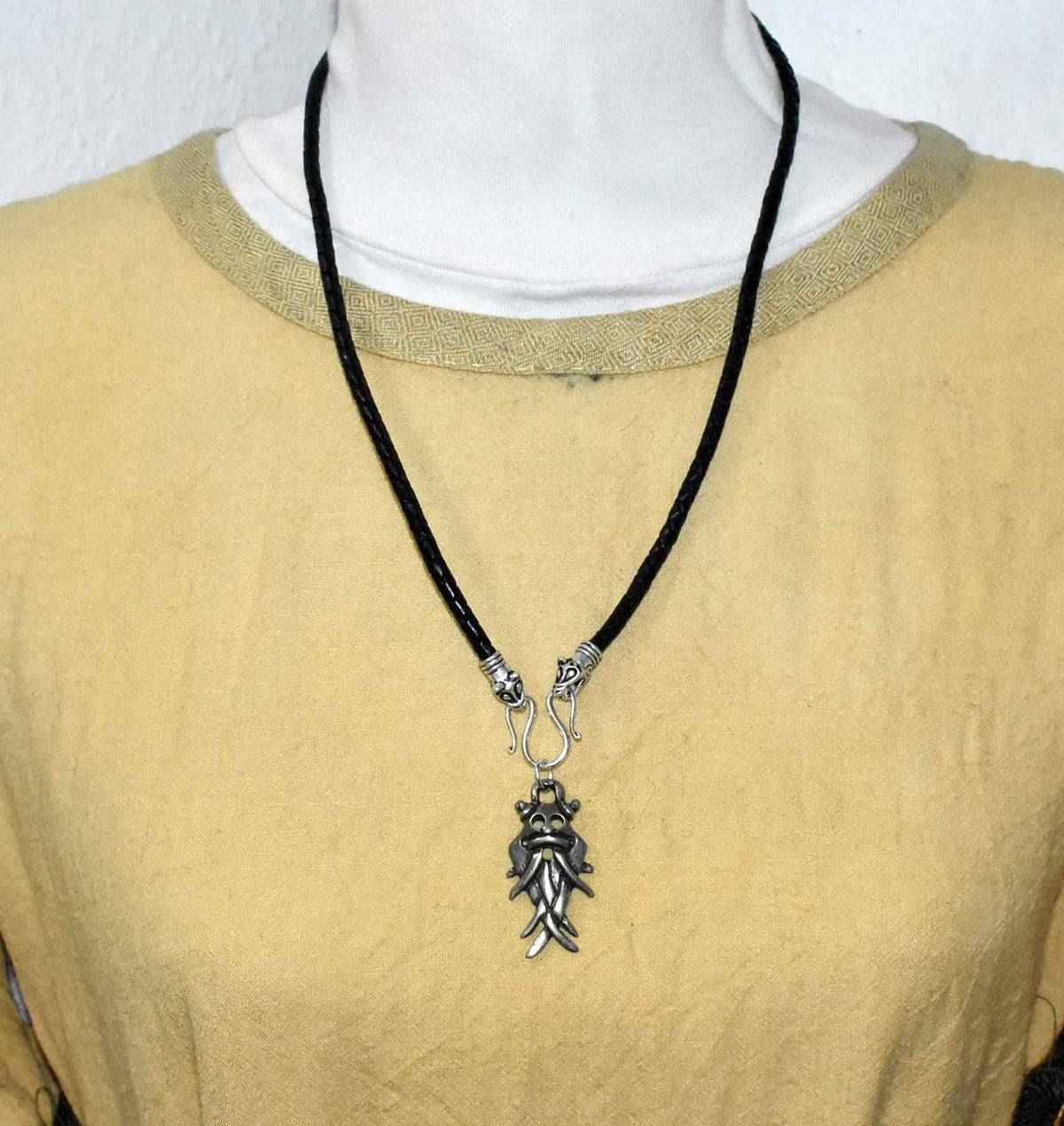 Tragebild der langen Aarhus-Masken-Kette schwarz mit silber am geflochtenen Lederband

Der Maskenanhänger aus ZAMAK hängt an einem Omega-Haken zwischen zwei dekorativen Tierkopfabschlüssen. 